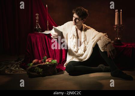 Ritratto artistico di giovane bell'uomo in immagine di famoso carattere storico, persona medievale isolata su sfondo vintage scuro. Stile retrò Foto Stock