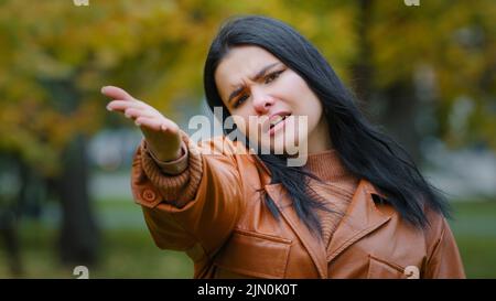 Giovane donna ispanica frustrato punta con la direzione della palma alla macchina fotografica dice hey voi insistentemente chiamata disperata ragazza sconvolta impressionabile si leva in piedi all'aperto Foto Stock