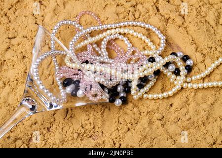 Bicchiere da cocktail con collane di perle sulla sabbia. Accessori sulla spiaggia. Foto Stock