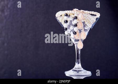 Bicchiere da cocktail pieno di perle e gioielli. Primo piano perls su sfondo scuro. Foto Stock