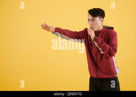 Accigliato allenatore fischio e gesturante a mano, isolato su giallo Foto Stock