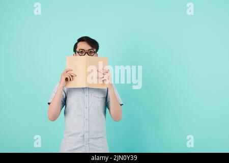 Ritratto di giovane uomo in bicchieri con cornici spesse che coprono metà del viso con libro Foto Stock