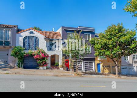 Fila di case inclinate a San Francisco, California, con alberi e piante vicino al marciapiede. Facciata di case con garage annesso vicino alle sue porte anteriori Foto Stock