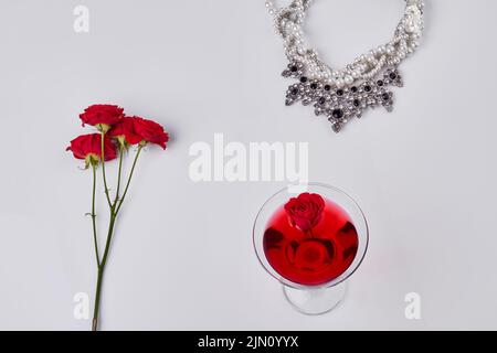 Cocktail rosso con fiori di rosa e collana. Vista dall'alto, disposizione piatta. Isolato su bianco. Foto Stock