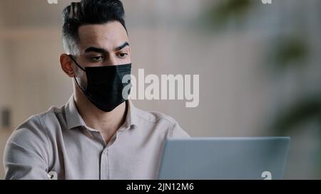 Arabian Sick uomo d'affari in maschera medica designer programmatore digitando su laptop di ricerca informazioni in rete sviluppare progetto di avvio chat in linea Foto Stock