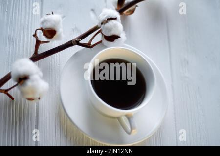 Tazza di caffè con ramo di fiori di cotone. Scrivania in legno bianco. Foto Stock