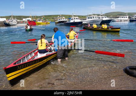 Barca a remi con equipaggio femminile in fase di lancio. Regata di Portmagee, Contea di Kerry, Irlanda Foto Stock