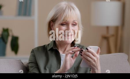 Primo piano felice eccitato successo stupito vecchia donna emotiva ricevere buone notizie offrire denaro premio obiettivo con telefono sorridente gioire mostrando pollice Foto Stock