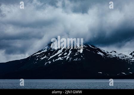 Vista del Monte Carlisle coperto di neve sotto le fitte nuvole sull'isola di Carlisle, una delle isole di quattro montagne del sottogruppo dell'arcipelago Aleutiano Foto Stock