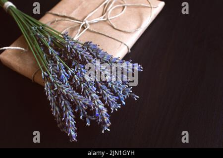 Confezione regalo di carta artigianale con fiori freschi su sfondo nero. Foto Stock