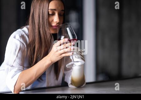 La ragazza calma e premurosa tiene un bicchiere di vino in braccio bionico a casa, donna con arto protesico artificiale. Foto Stock