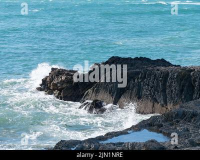 Le onde di marea si infrangono sulle rocce costiere, sul mare. L'acqua è di colore turchese. Schiuma bianca sulle onde, spruzzi, roccia accanto al mare. Foto Stock