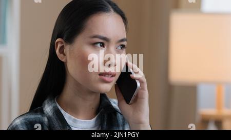 Triste donna asiatica millennial confuso ragazza arrabbiata in casa parlando al telefono rispondere chiamata preoccupazioni circa cattive notizie problemi di rete problemi cellulari Foto Stock