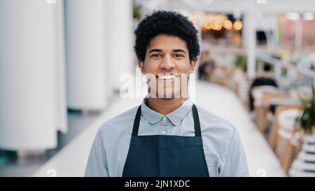 Ritratto maschile sorridente felice amichevole African cafe pub lavoratore biraciale professionista uomo cameriere in grembiule uniforme piccolo imprenditore posa al coperto Foto Stock