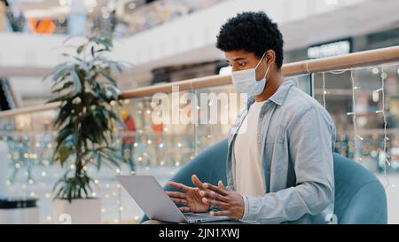 African american uomo in faccia medico maschera ufficio azienda luogo di lavoro videochiamata con portatile covid epidemia online insegnante tutor consulente remoto Foto Stock
