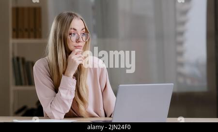 Caucasica millennial business donna studentessa ragazza scrittore giornalista indossare occhiali seduti al tavolo in ufficio a casa con laptop pensa idea Foto Stock