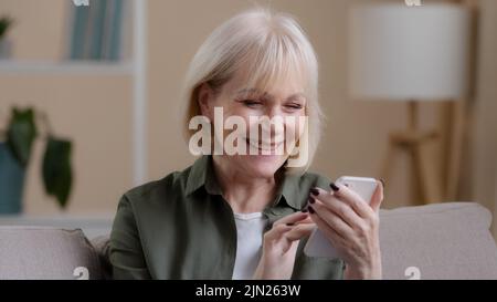 Primo piano felice sorridendo riuscito stupito vecchia donna impressionabile ricevere buone notizie offrire il premio di denaro obiettivo con telefono sorridente gioire mostrando pollice Foto Stock