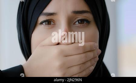Ritratto femminile al coperto Islamic Arabian ragazza triste paura musulmana donna araba donna in nero hijab guardando la macchina fotografica copre la bocca con mani silenzio tranquillo Foto Stock