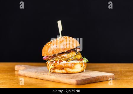 Close-up di freschi e deliziosi fatti in casa burger con lattuga, formaggio, cipolla e pomodoro su un rustico di asse di legno su uno sfondo scuro Foto Stock