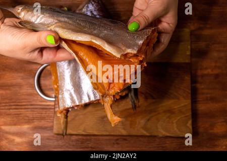 primo piano della carcassa di salmone con filetto sullo sfondo di un tagliere, le mani femminili lo tengono Foto Stock