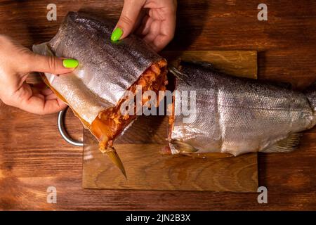nelle mani di una carcassa di salmone sullo sfondo di un tagliere Foto Stock