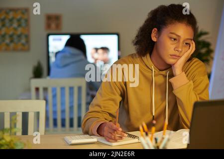 Studentessa annoiato e stanca che guarda il webinar su un notebook e prende appunti in un manuale Foto Stock
