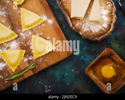 Cucina ravioli italiani fatti in casa da pasta con ripieno di carne. Ravioli su un tagliere, ingredienti su sfondo marmoreo. Ricette per il ristorante Foto Stock