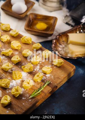 Piccoli ravioli crudi fatti in casa, gnocchi su un tagliere di legno su sfondo blu scuro. Processo di cottura. Deliziosi piatti fatti in casa, tradizioni familiari Foto Stock