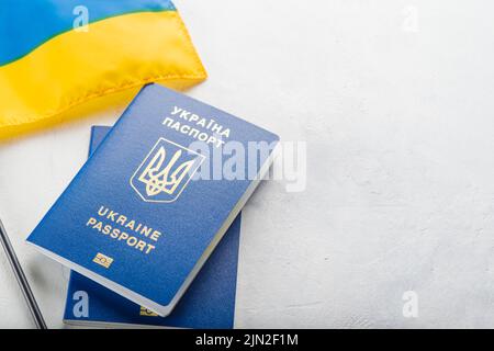 Su sfondo bianco ci sono due passaporti biometrici ucraini e una piccola bandiera Ucraina. Patriottismo, democrazia, libertà, costituzione. Turismo, viaggi Foto Stock