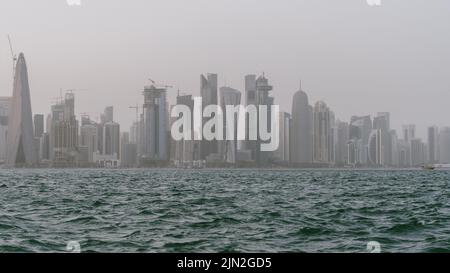 Skyline del Qatar con mare ruvido in primo piano in una giornata ventosa e piovosa. Foto Stock