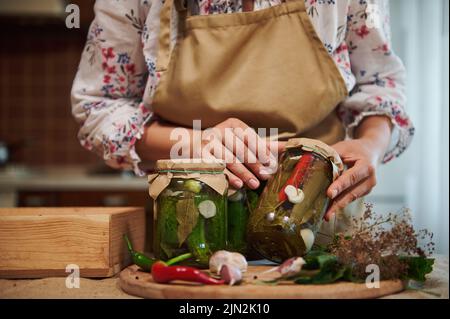 Primo piano di cetrioli e peperoncini sott'aceto fatti in casa in vasetti di vetro sterilizzati in mani femminili Foto Stock