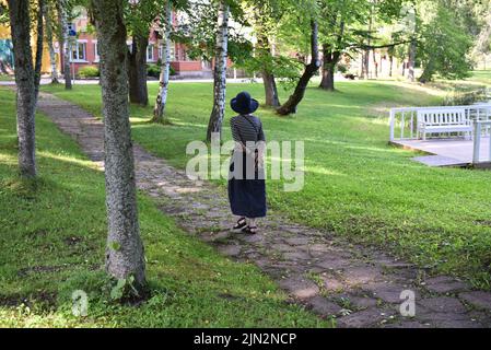 Una donna in un cappello cammina nel parco. Vista dal retro. Foto Stock