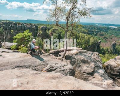 Schmilka - Germania, 06 luglio 2022: Tourist with camera sta scattando foto dietro il massiccio roccioso di Schrammsteine, Sassonia Svizzera, Germania. Vista dal Th Foto Stock