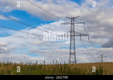 Linee elettriche ad alta tensione e piloni di potenza in un paesaggio agricolo in una giornata di sole con le nuvole di cirrus nel cielo blu. Foto Stock