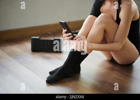 Immagine ritagliata della ballerina seduta sul pavimento in studio e scelta della musica su smartphone a cui ballare Foto Stock