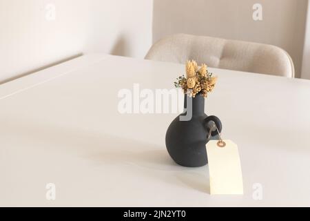 Sfondo interno di moderna camera vuota con parete bianca, vaso nero con fiore secco e tavolo in legno, spazio copia. Foto Stock
