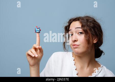 La giovane donna tiene il pupazzo di un virus COVID-19 sul suo dito senza paura; concetto della nuova normalità e del potere della scienza e della conoscenza Foto Stock