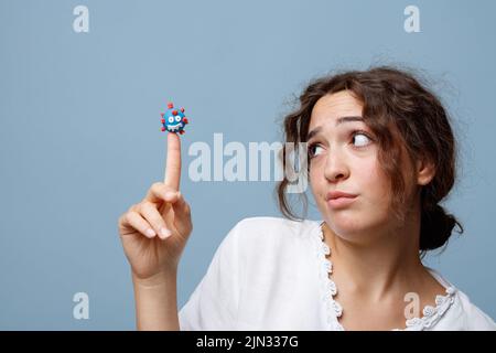 La giovane donna tiene il pupazzo di un virus COVID-19 sul suo dito senza paura; concetto della nuova normalità e del potere della scienza e della conoscenza Foto Stock