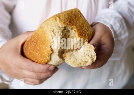 Un uomo tiene il pane cotto nelle sue mani, strappa un pezzo da esso. Cibo Foto Stock