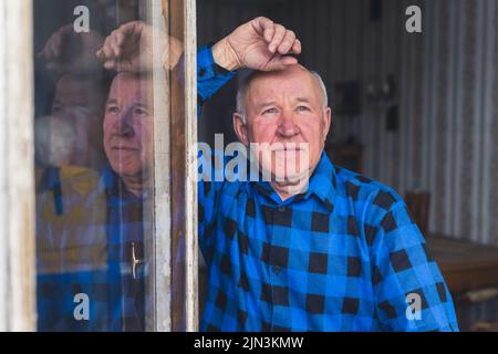 Vecchio caucasico pensionato uomo grigio-capelli fissando fuori la finestra aperta. Foto di alta qualità Foto Stock