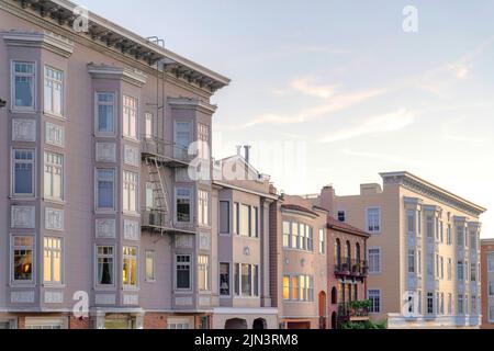 Appartamenti vittoriani e case cittadine con riflesso del tramonto sulle sue finestre a San Francisco, CA. Ci sono case cittadine nel mezzo di due appartamenti Foto Stock
