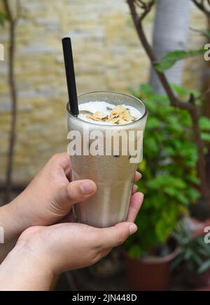 Le mani che tengono il bicchiere con il latte di caffè scuotono con cocco bruciato Foto Stock