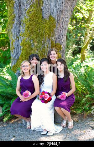 Bella sposa giovane biraciale sorridente con il suo gruppo multietnico di quattro bridesmaids in abiti viola Foto Stock