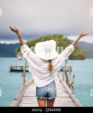 Ho aspettato così tanto per questa vacanza. Dietro l'inquadratura di una donna irriconoscibile in piedi con le braccia sollevate su una passerella che si affaccia sul mare durante Foto Stock