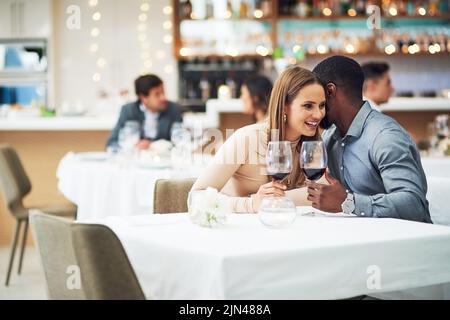 HES mai così naughty. Un giovane affettuoso sussurrando nel suo orecchio delle girlfriends mentre si siede in un ristorante. Foto Stock