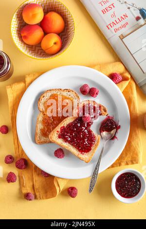 Piatto con gustosi toast, albicocca e marmellata di lamponi su sfondo giallo Foto Stock