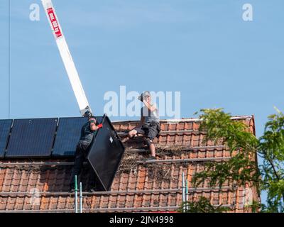 Sint Gillis WAAS, Belgio, 08 agosto 2022, Roofer siede sul tetto e solleva il pollice alla telecamera mentre un altro tetto sta tenendo un pannello solare Foto Stock
