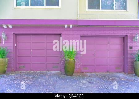 Garage viola esterno di due case cittadine con piante in vaso vicino ai mattoni dipinti-San Francisco, CA. Due porte da garage sezionali con lampade da parete sul Foto Stock