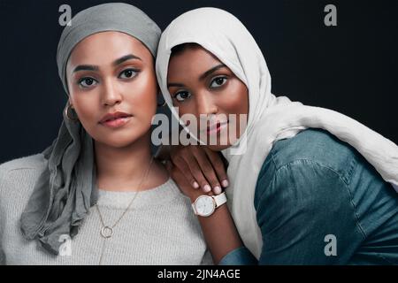 Siate sempre fieri della persona che siete. Due giovani donne attraenti che indossano i hijab e che si levano in piedi insieme contro uno sfondo nero in Foto Stock