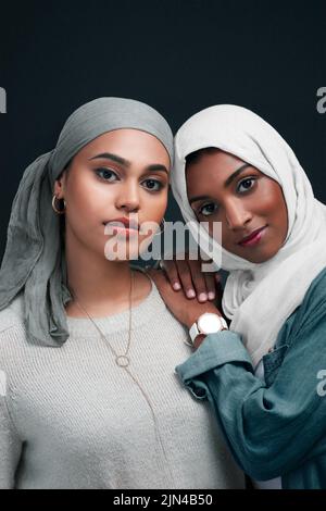 Proteggersi l'un l'altro, sempre. Due giovani donne attraenti che indossano i hijab e che si levano in piedi insieme contro uno sfondo nero nello studio. Foto Stock